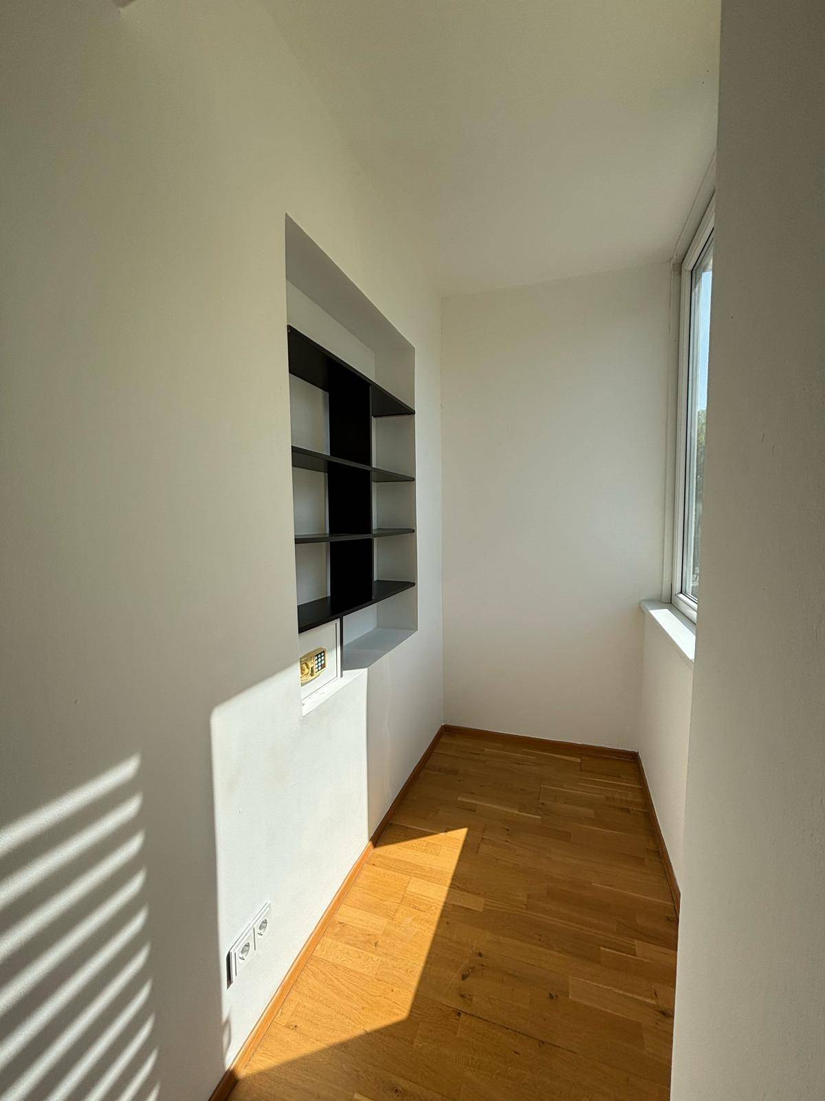 Heller Nischenbereich mit eingebauten Regalen und Fenster, durchflutet von Sonnenlicht.