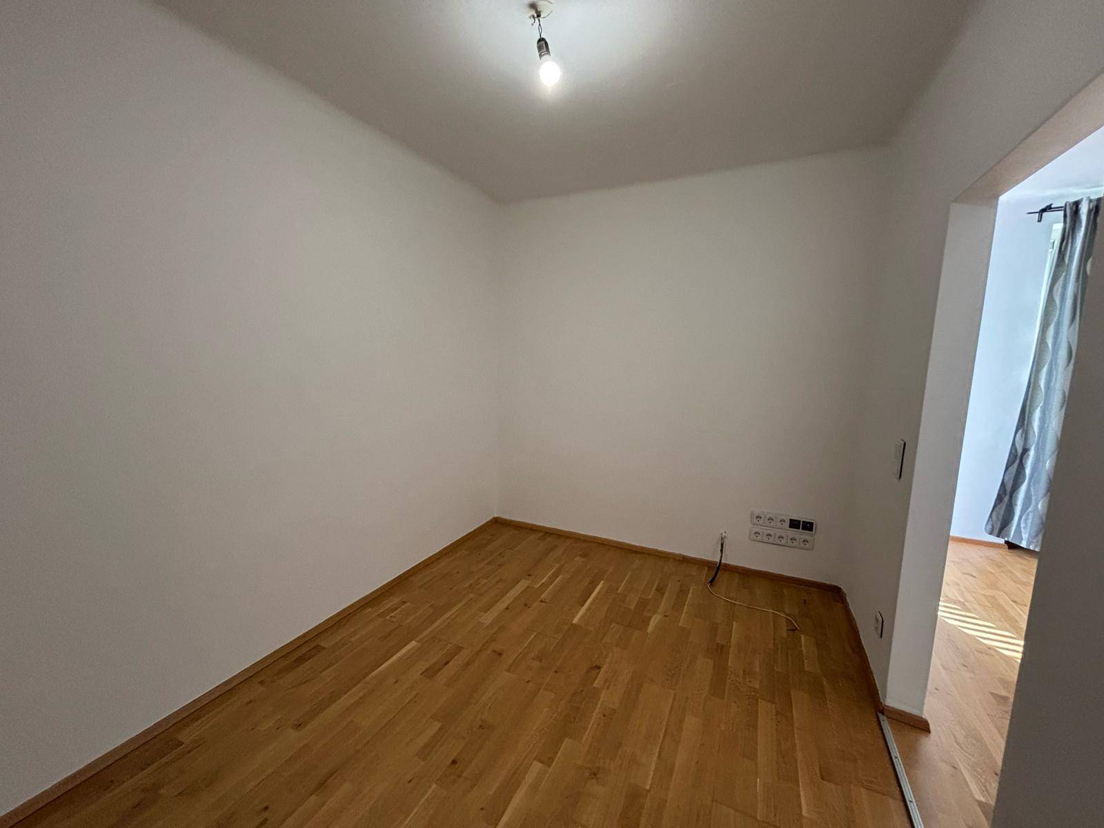 Leeres Zimmer mit Parkettboden und weiß gestrichenen Wänden, bereit zur Einrichtung.