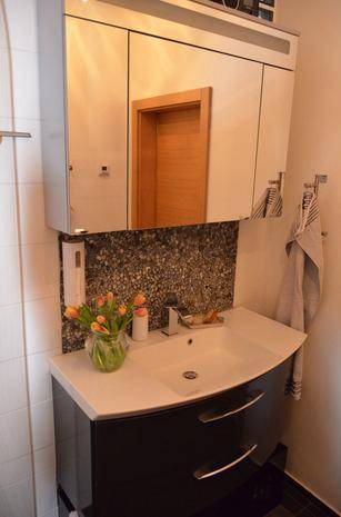 Badezimmer mit modernem Waschtisch, Spiegel und Blumenarrangement.