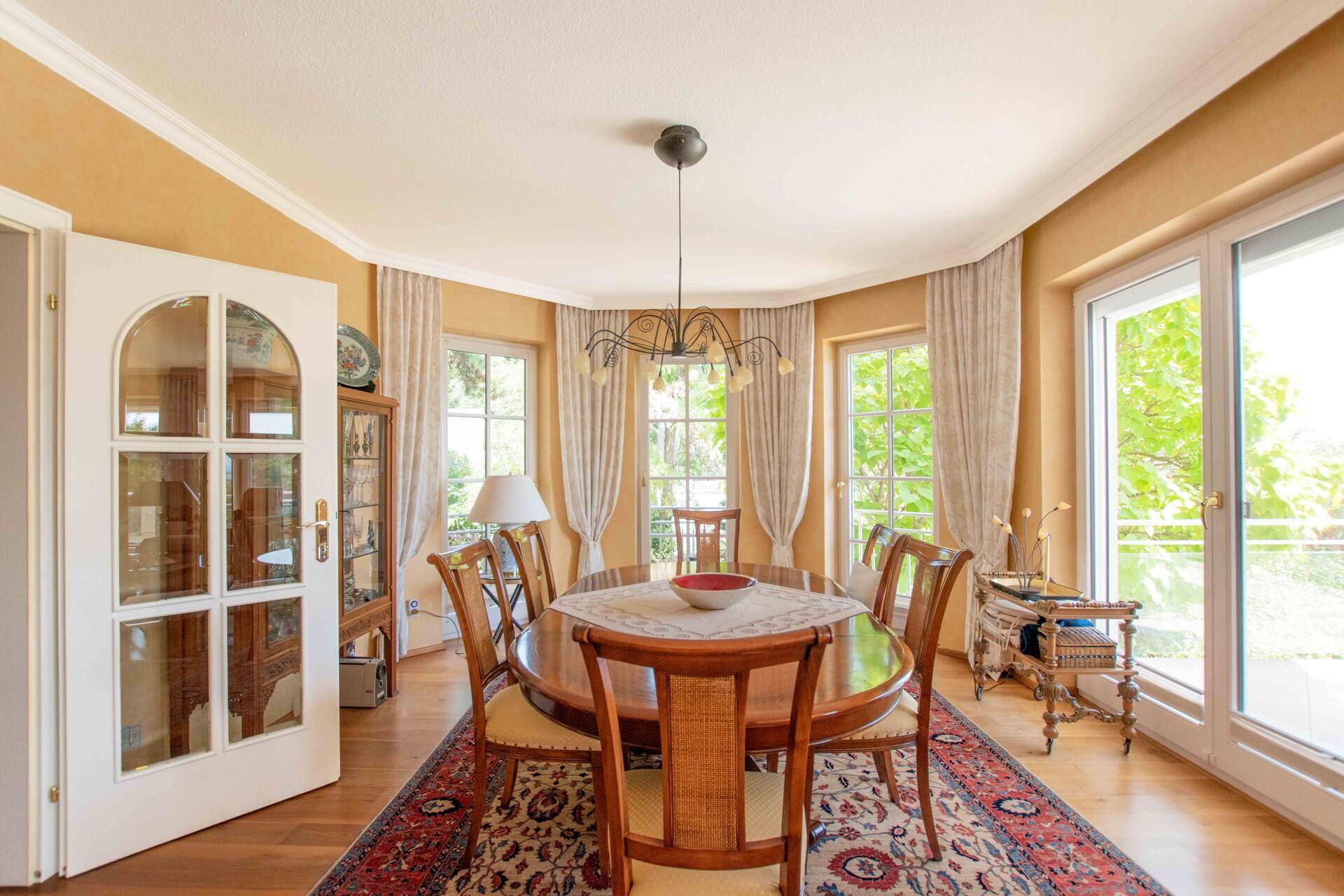 Eleganter Essbereich mit großem Holztisch, Parkettboden und vielen Fenstern für viel Licht.