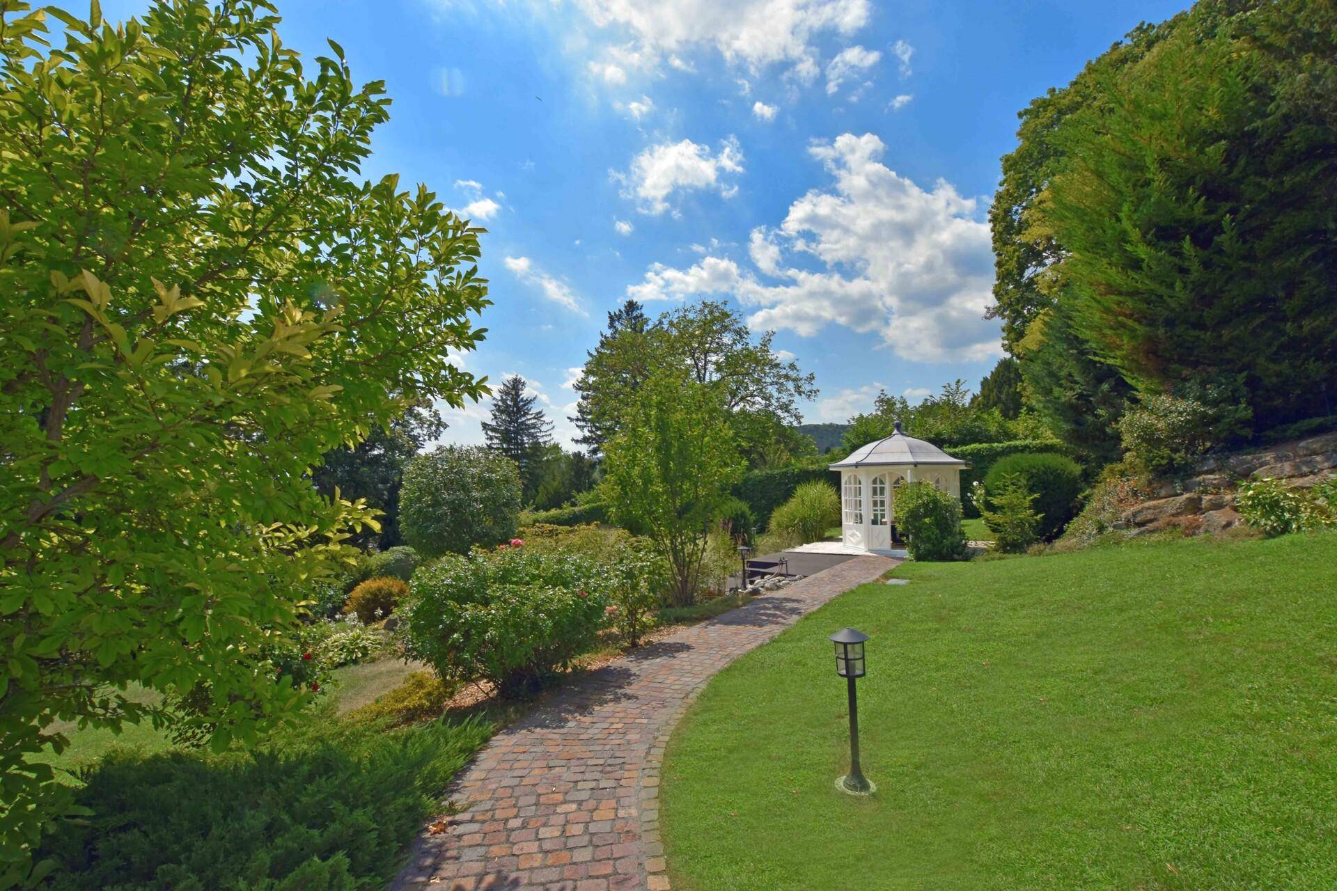 Idyllischer Gartenweg führt zu einem charmanten weißen Gartenpavillon unter blauem Himmel.