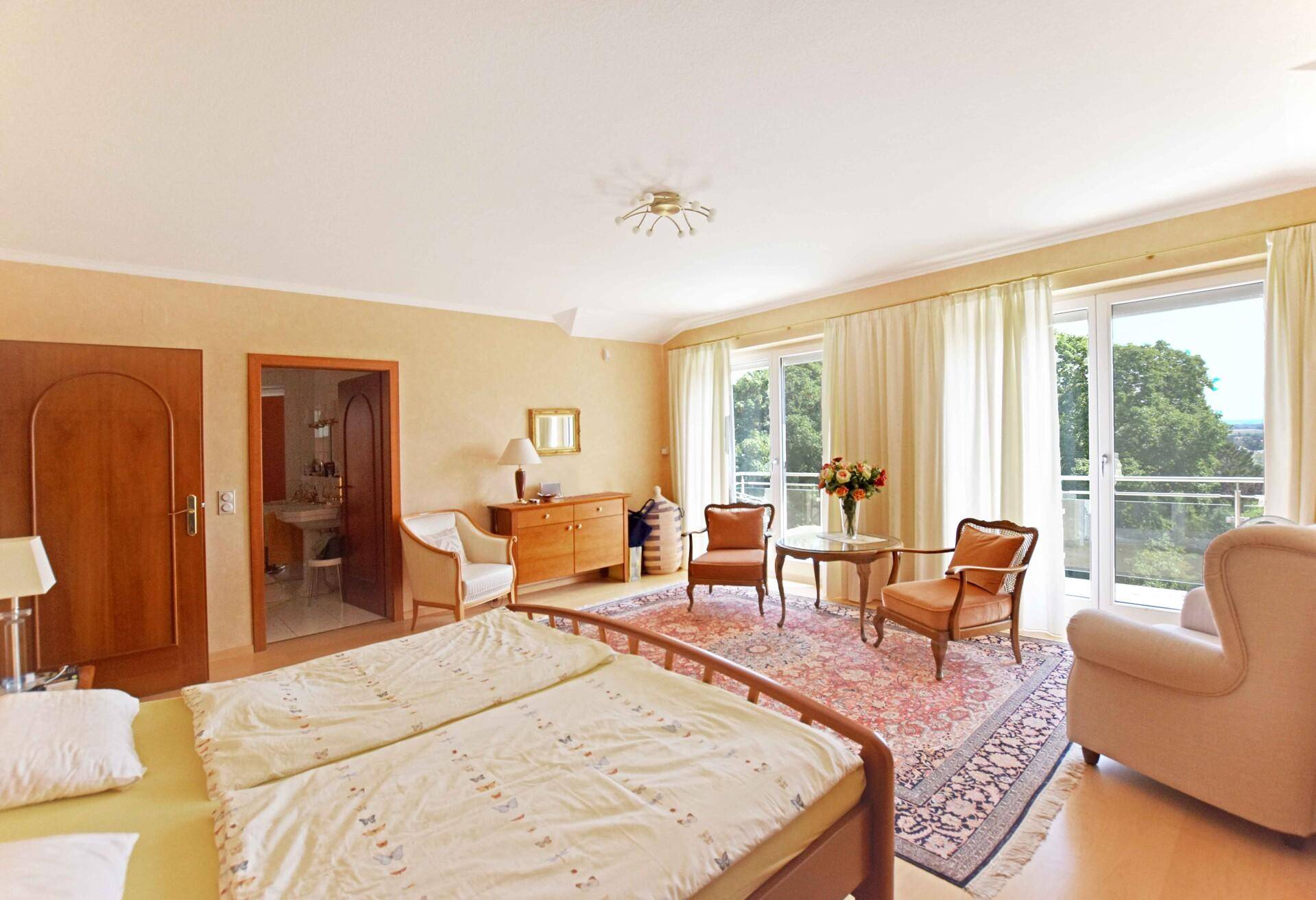 Geräumiges Schlafzimmer mit Balkonzugang, Sitzbereich und Blick auf die Landschaft.