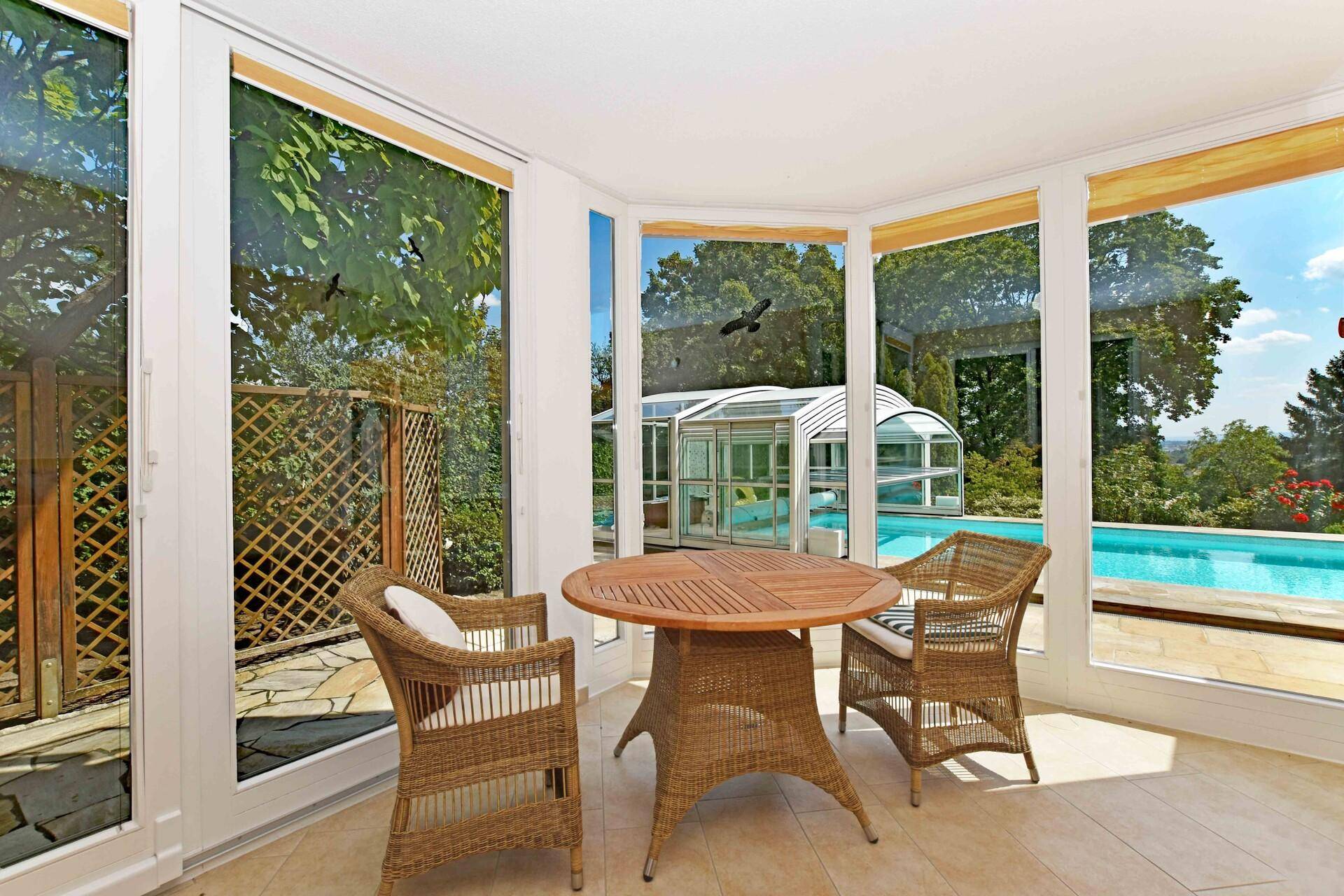 Heller Wintergarten mit Rattanmöbeln und direktem Blick auf den Swimmingpool und Garten.
