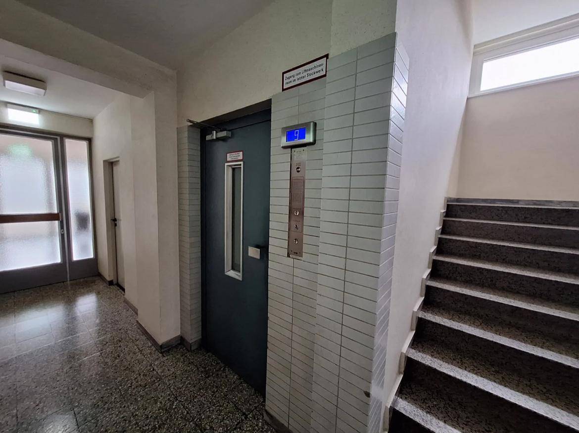 Treppenhaus mit Aufzug und gefliesten Wänden in einem Mehrfamilienhaus.