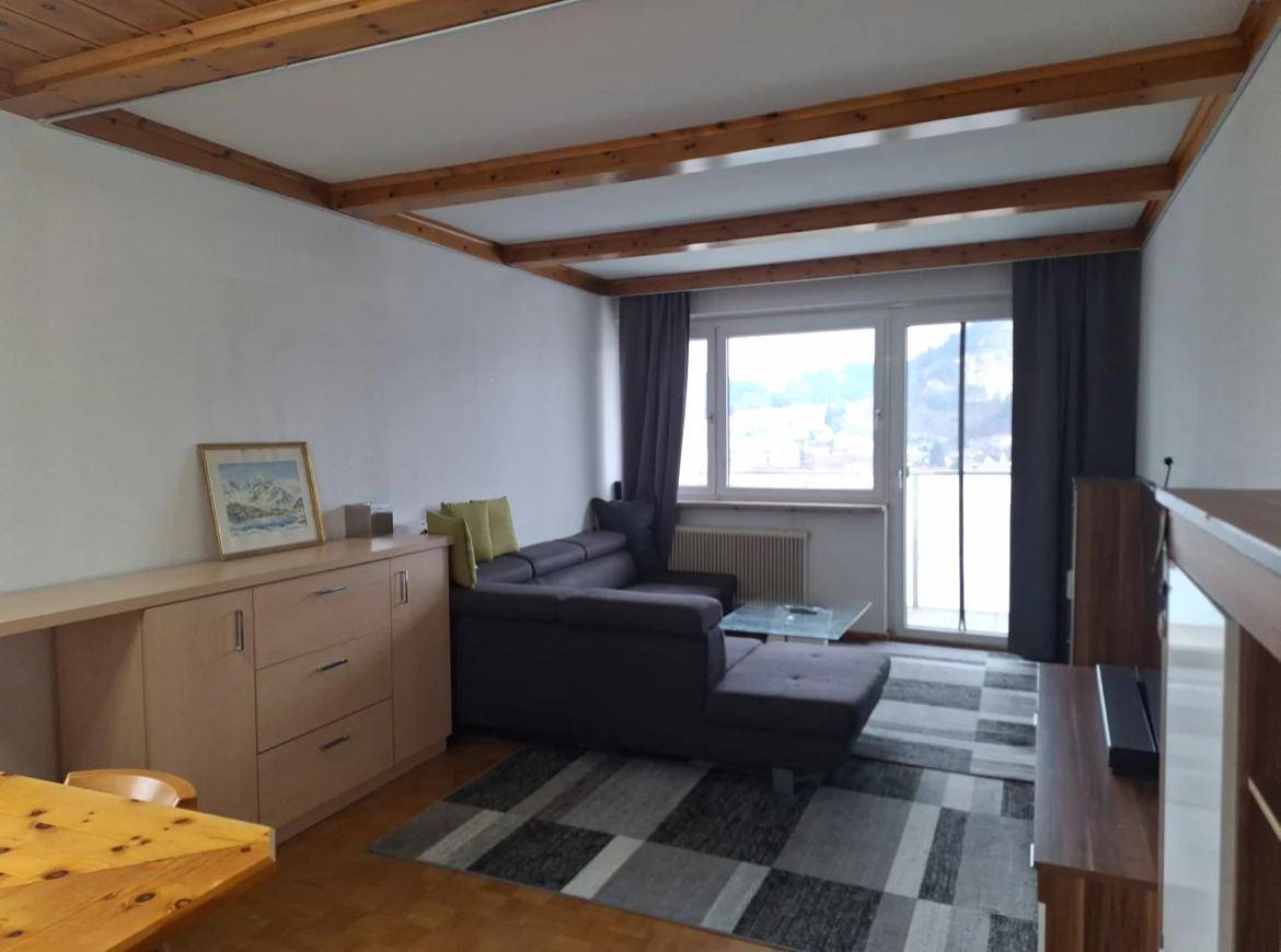 Geräumiges Wohnzimmer mit bequemer Couch, Holzbalkendecke und Zugang zum Balkon.