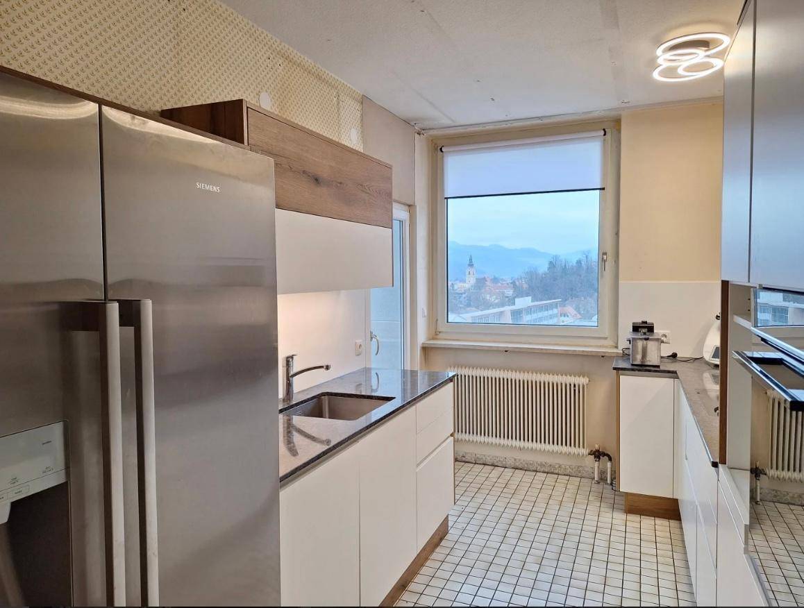 Moderne Küche mit weißen Schränken, dunkler Arbeitsplatte und großem Fenster mit Bergblick.