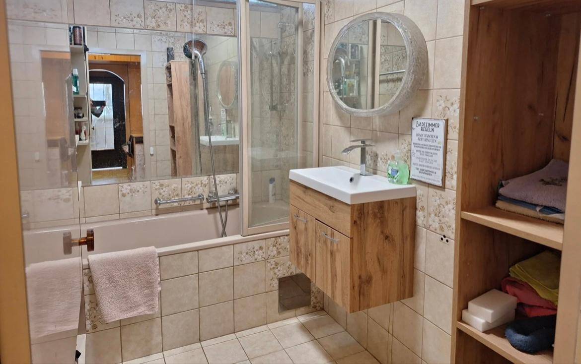Gefliestes Badezimmer mit Badewanne, Duschbereich und modernem Waschtisch.