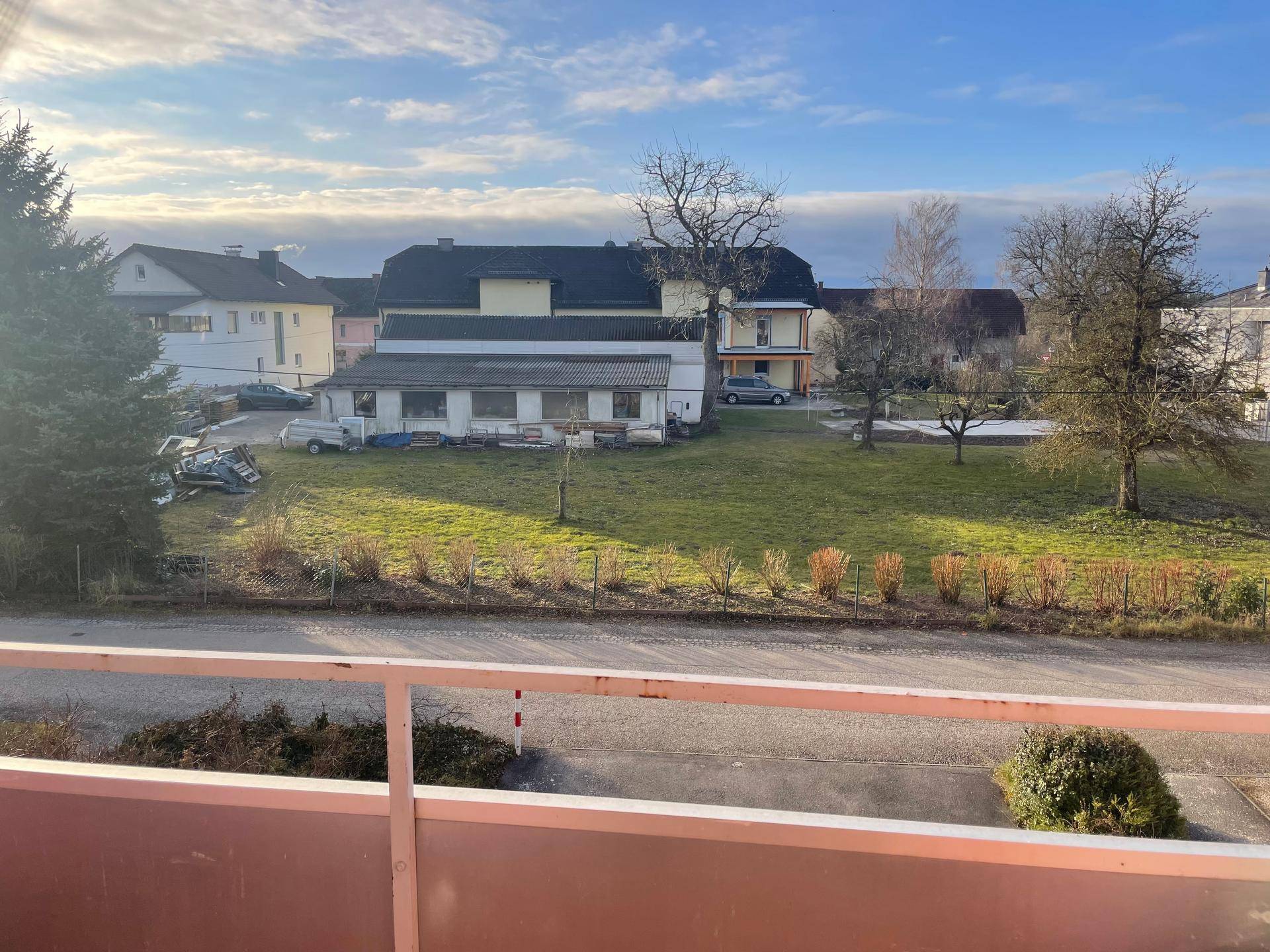 Weitläufiger Blick über eine grüne Landschaft mit Häusern und Bäumen unter einem bewölkten Himmel.