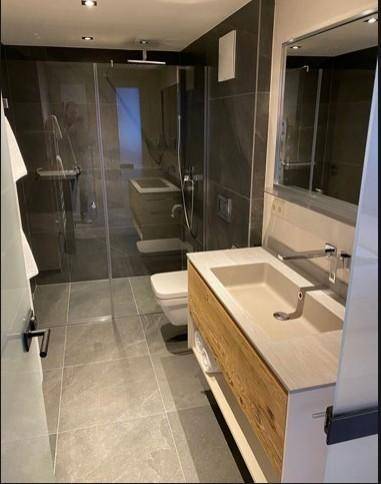 Modernes Badezimmer mit begehbarer Dusche, eleganten grauen Fliesen und einem Holzwaschtisch.