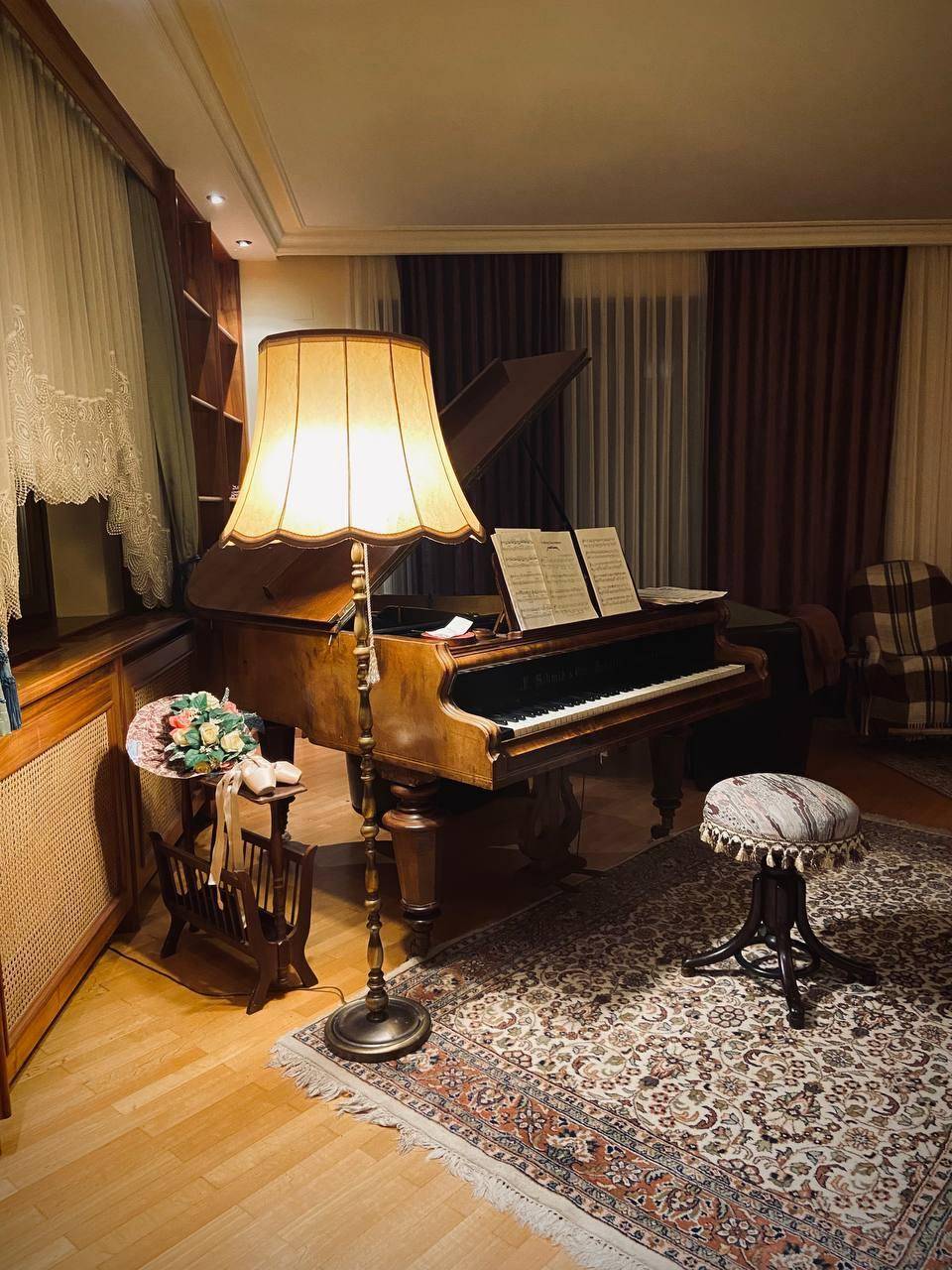 Klassisches Wohnzimmer mit Flügel, Teppichboden und warmem Licht einer Stehlampe.