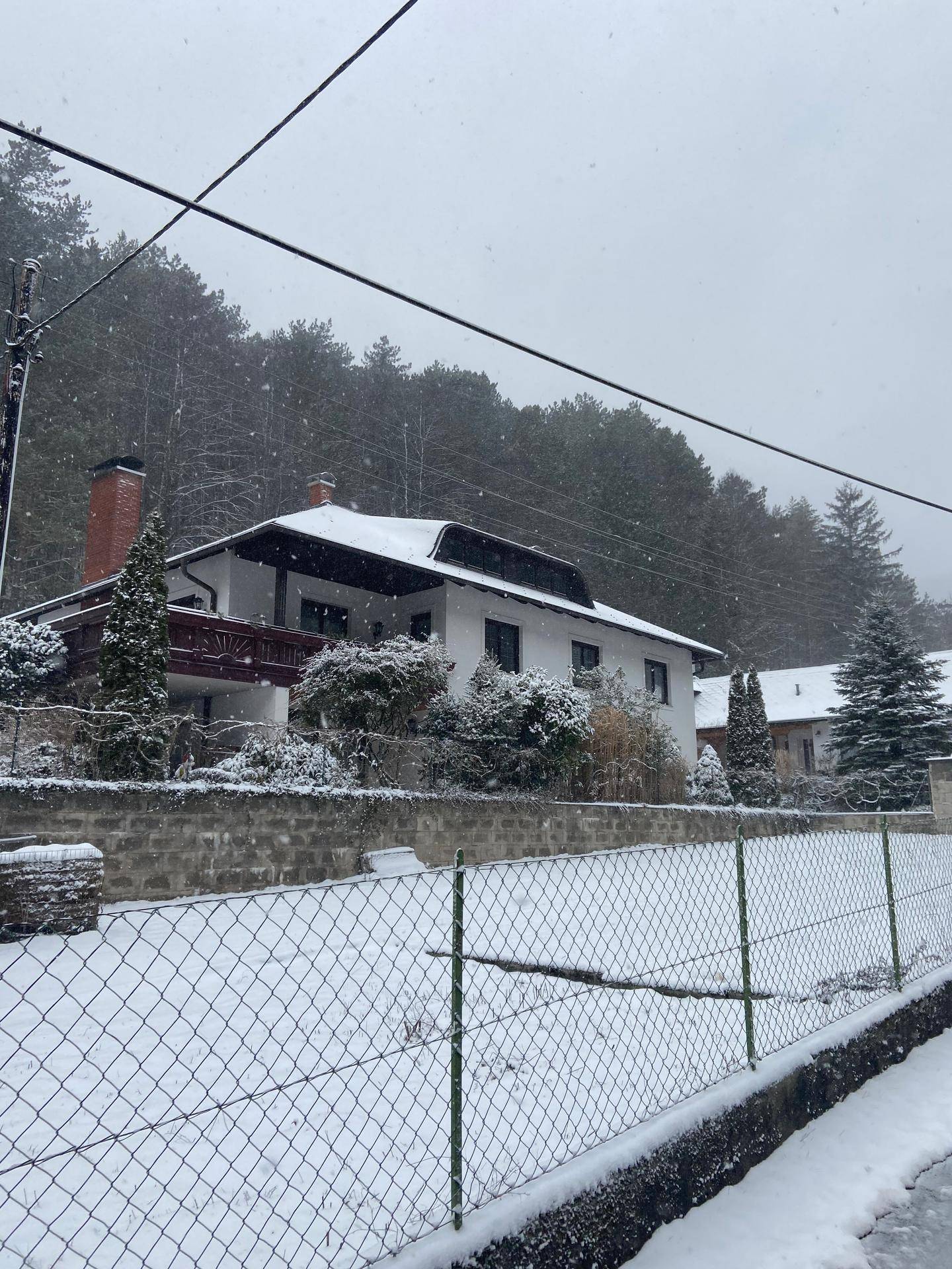 Hausfassade im Winter, umgeben von Schnee und verschneiten Bäumen.