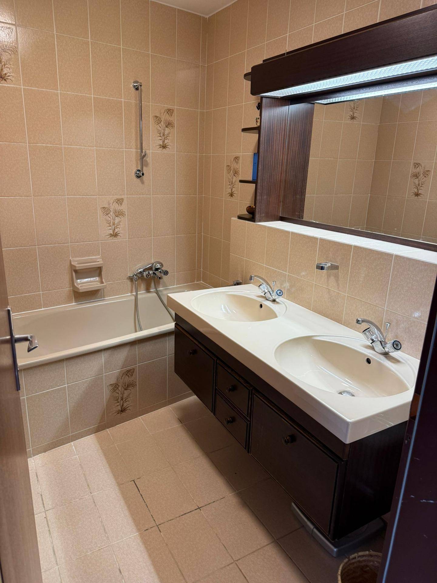 Badezimmer im Stil der 80er Jahre mit beigefarbenen Fliesen, Doppelwaschbecken und Badewanne.