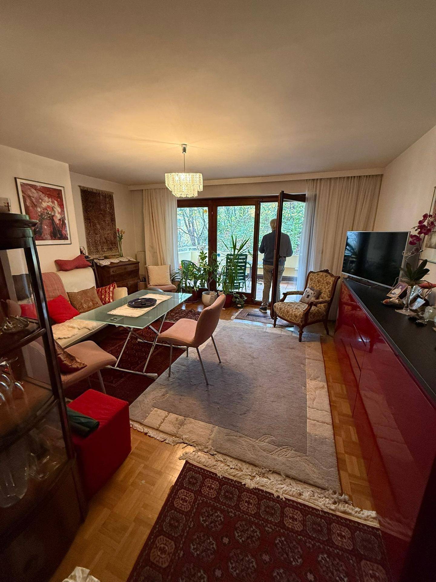 Gemütliches Wohnzimmer mit Parkettboden, farbenfroher Dekoration und Zugang zum Balkon.
