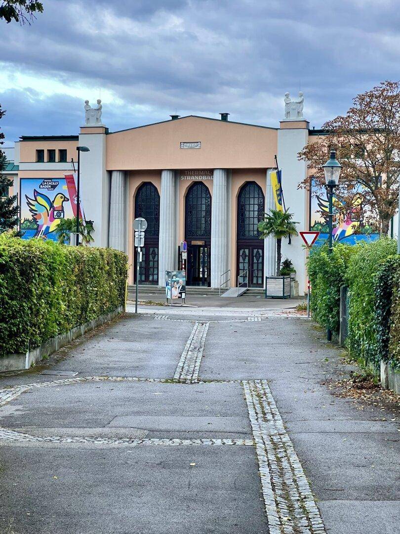 Historisches Gebäude mit großen Säulen und dekorativen Wandgemälden unter bewölktem Himmel.