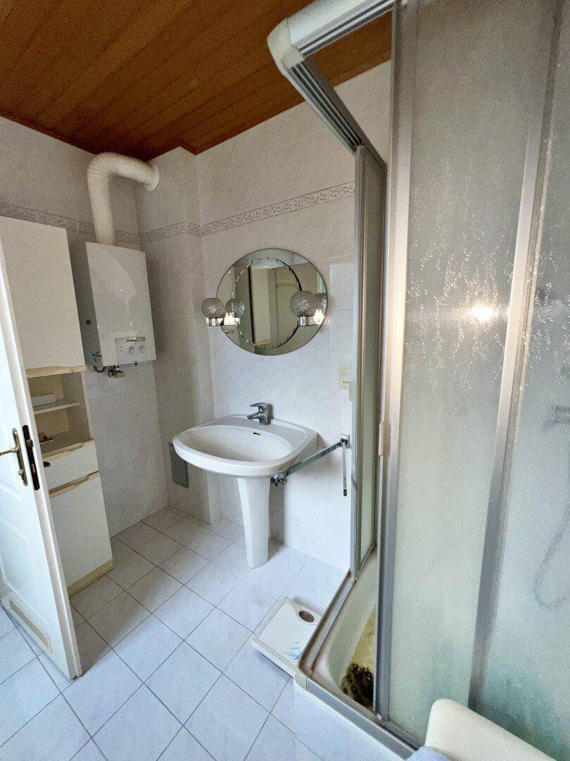 Badezimmer mit Duschkabine, Waschbecken, Spiegel und Holzdecke.