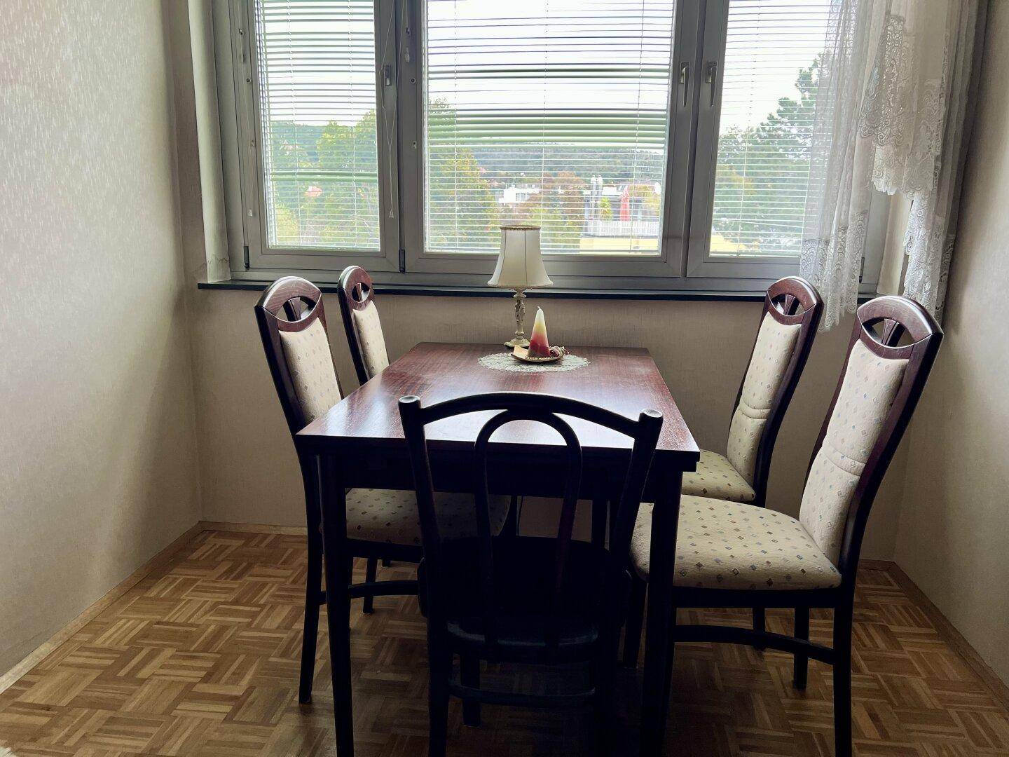 Essbereich mit Holztisch und Stühlen vor einem Fenster mit Jalousien.