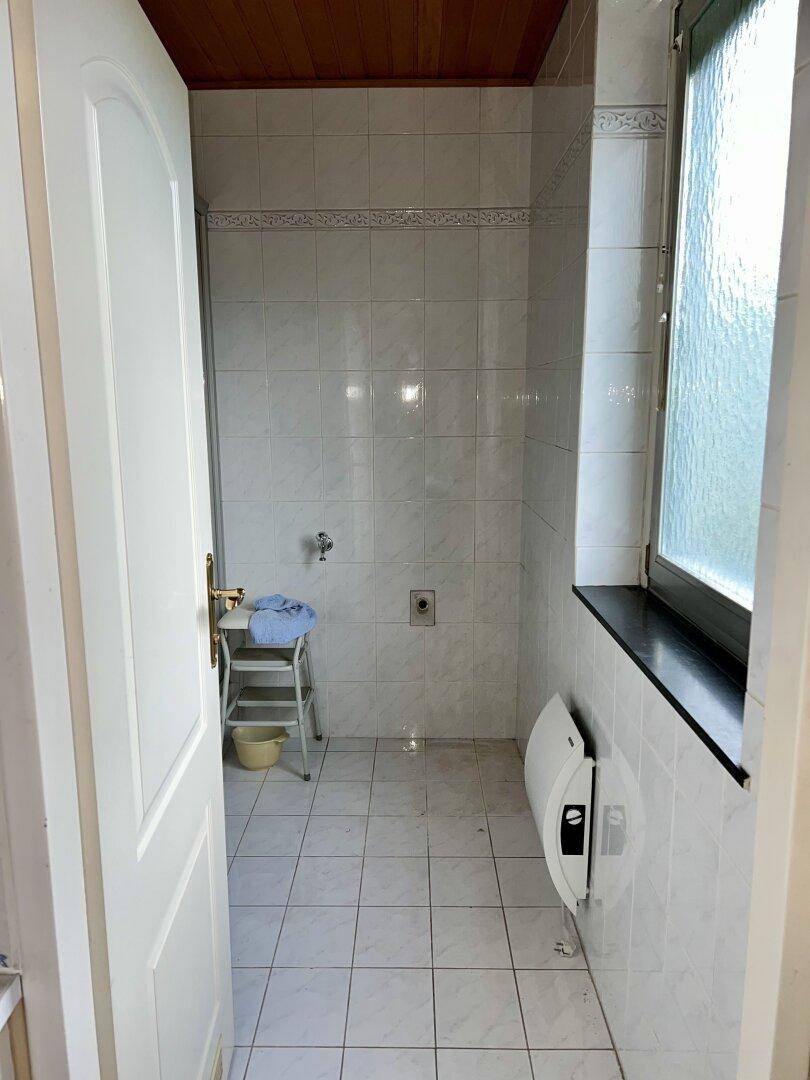 Gefliestes Badezimmer mit Fenster, Duschbereich und Holzdecke.