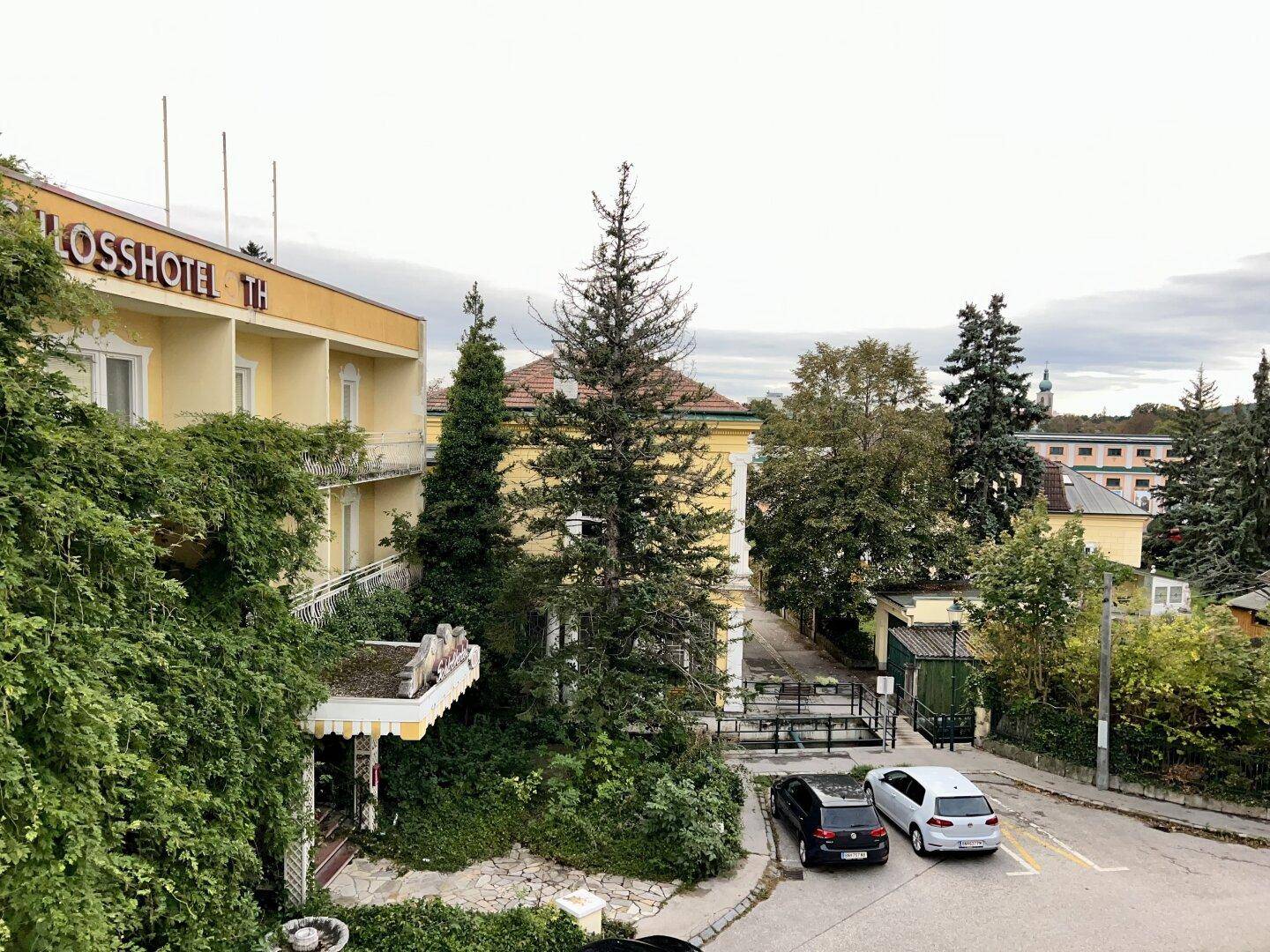 Blick auf ein gelbes Hotelgebäude und eine Straße mit parkenden Autos und Bäumen.