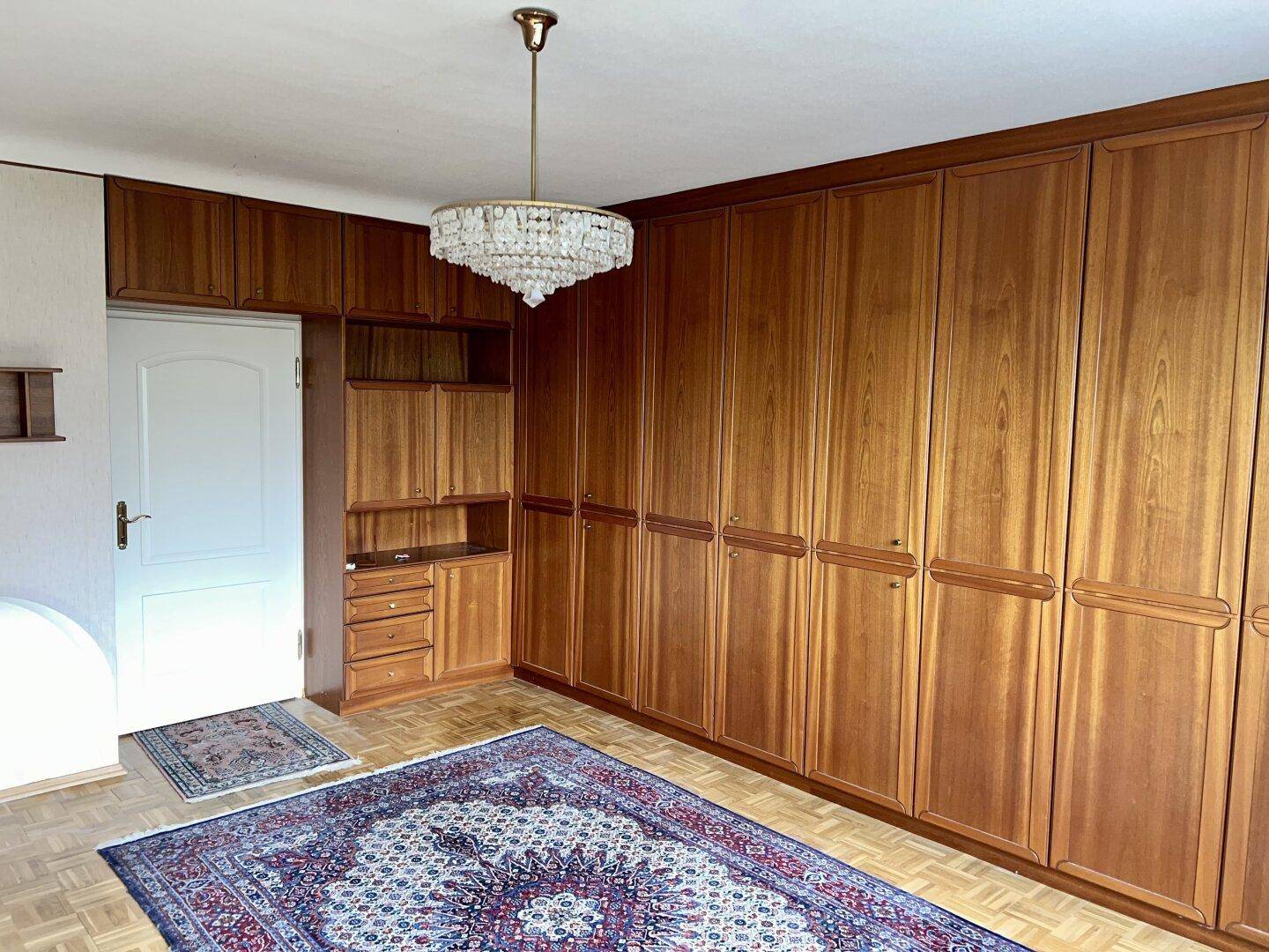 Schlafzimmer mit großen Einbauschränken aus Holz, Teppich und Kronleuchter.