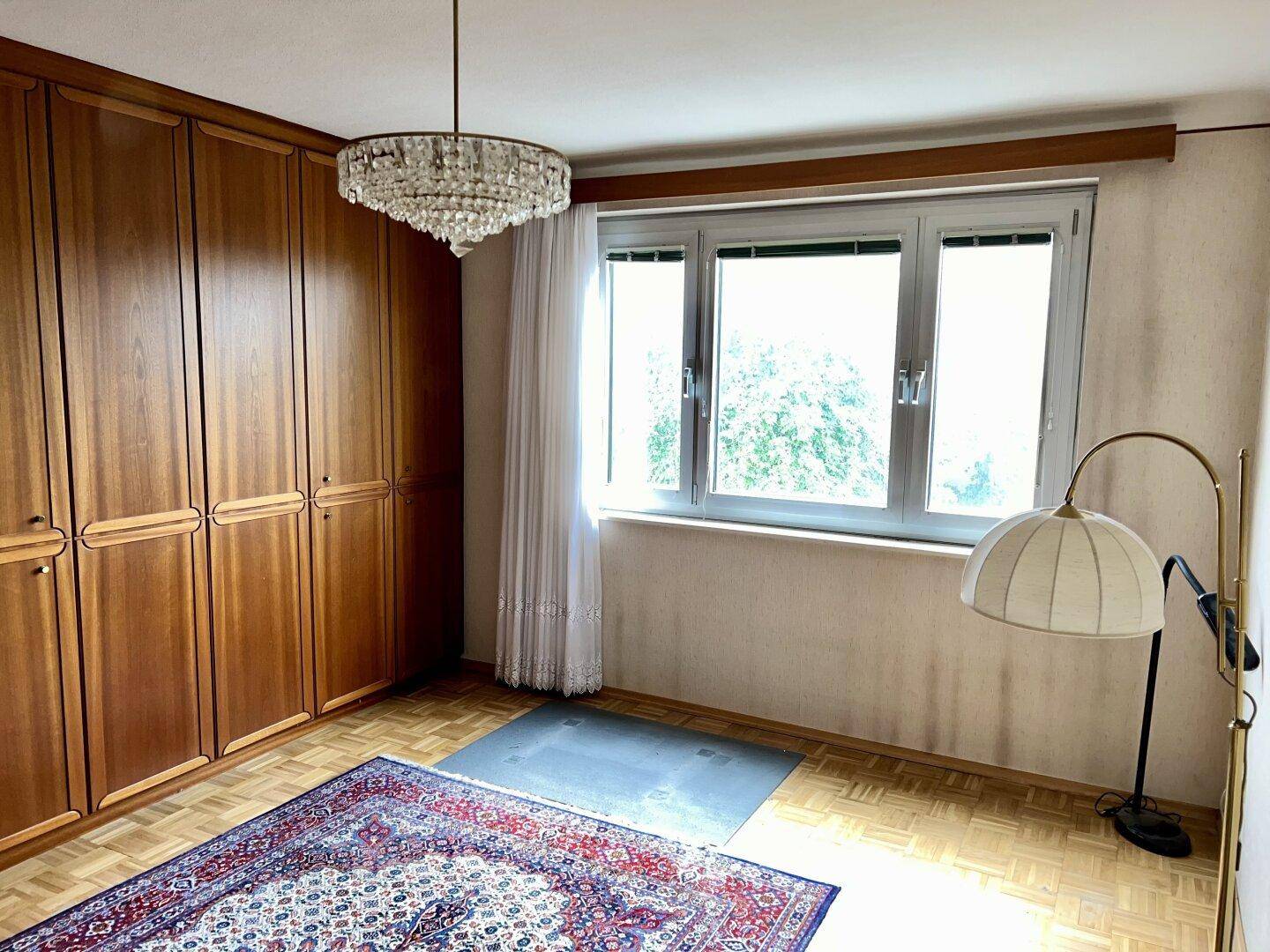 Helles Schlafzimmer mit Einbauschränken, Teppich und Fenster mit Blick ins Grüne.
