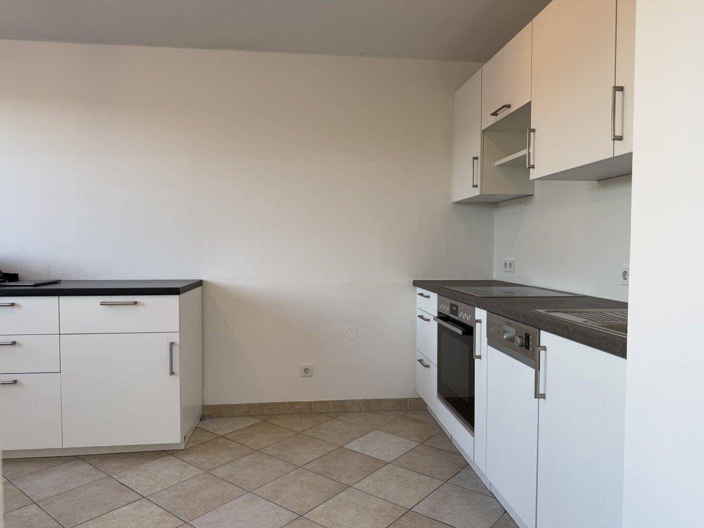 Moderne Einbauküche mit weißen Schränken, dunkler Arbeitsplatte und Fliesenboden.