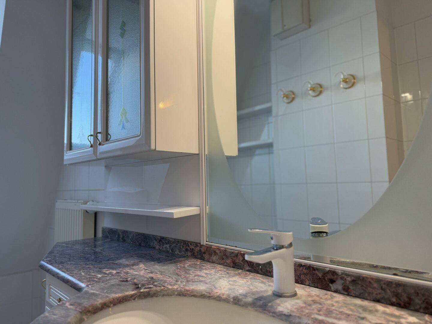 Badezimmer mit Marmorwaschtisch, Spiegelschrank und weißen Fliesen, in gutem Zustand.
