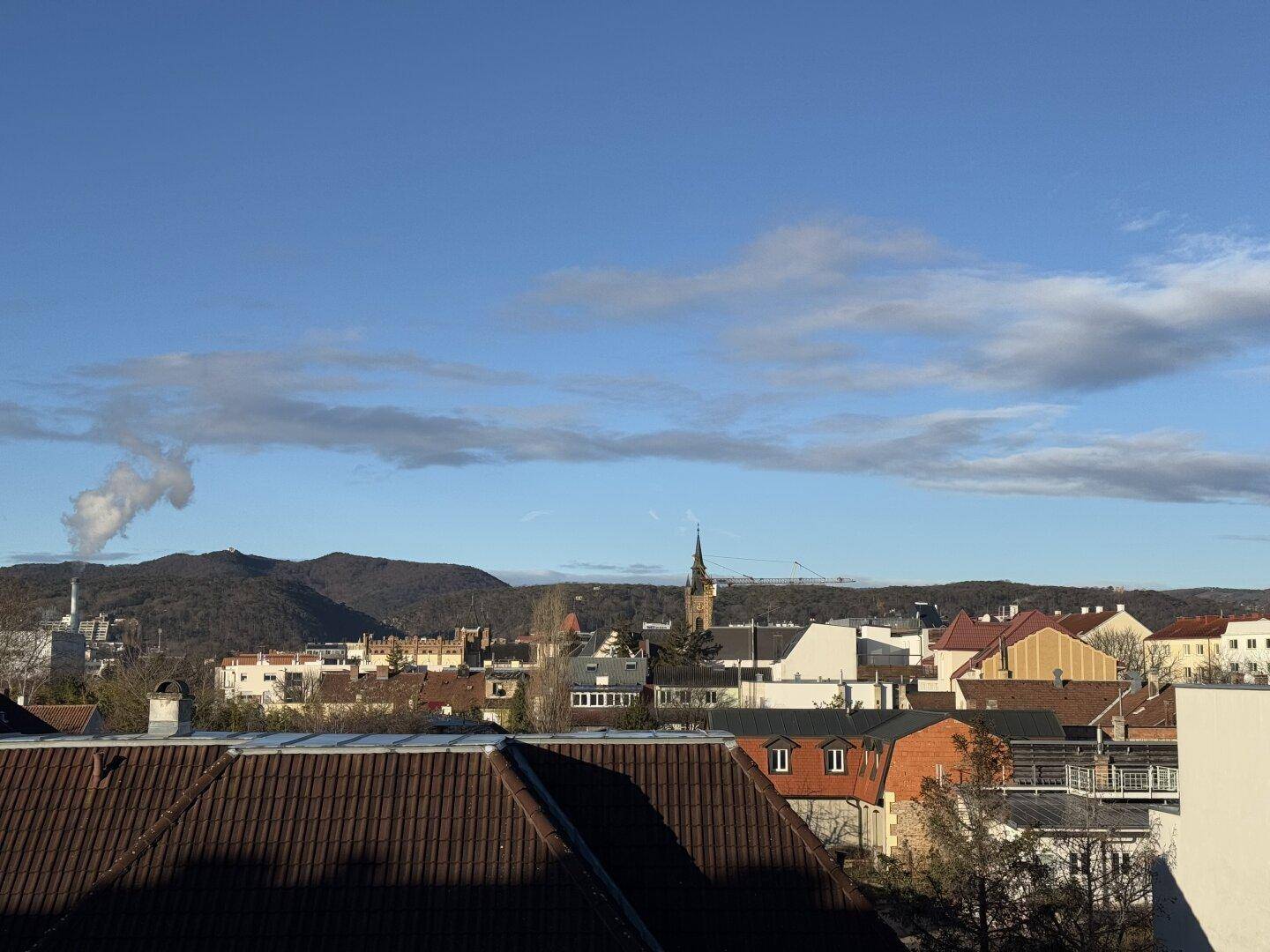 Weitblick über eine Stadt mit Dächern, Bergen und blauem Himmel im Hintergrund.