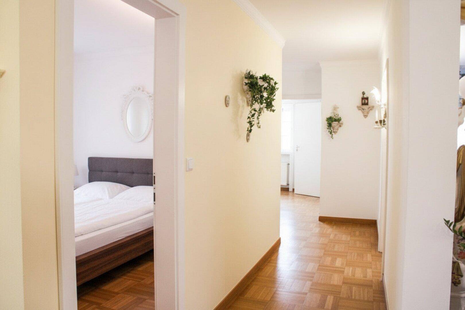 Heller Flur mit Parkettboden und Zugang zu einem Schlafzimmer.