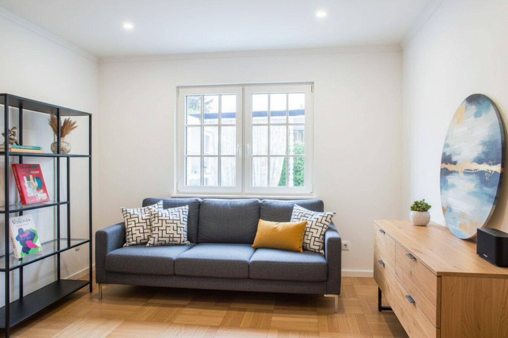 Modernes Wohnzimmer mit grauem Sofa, Holzkommode und schwarzem Regal.