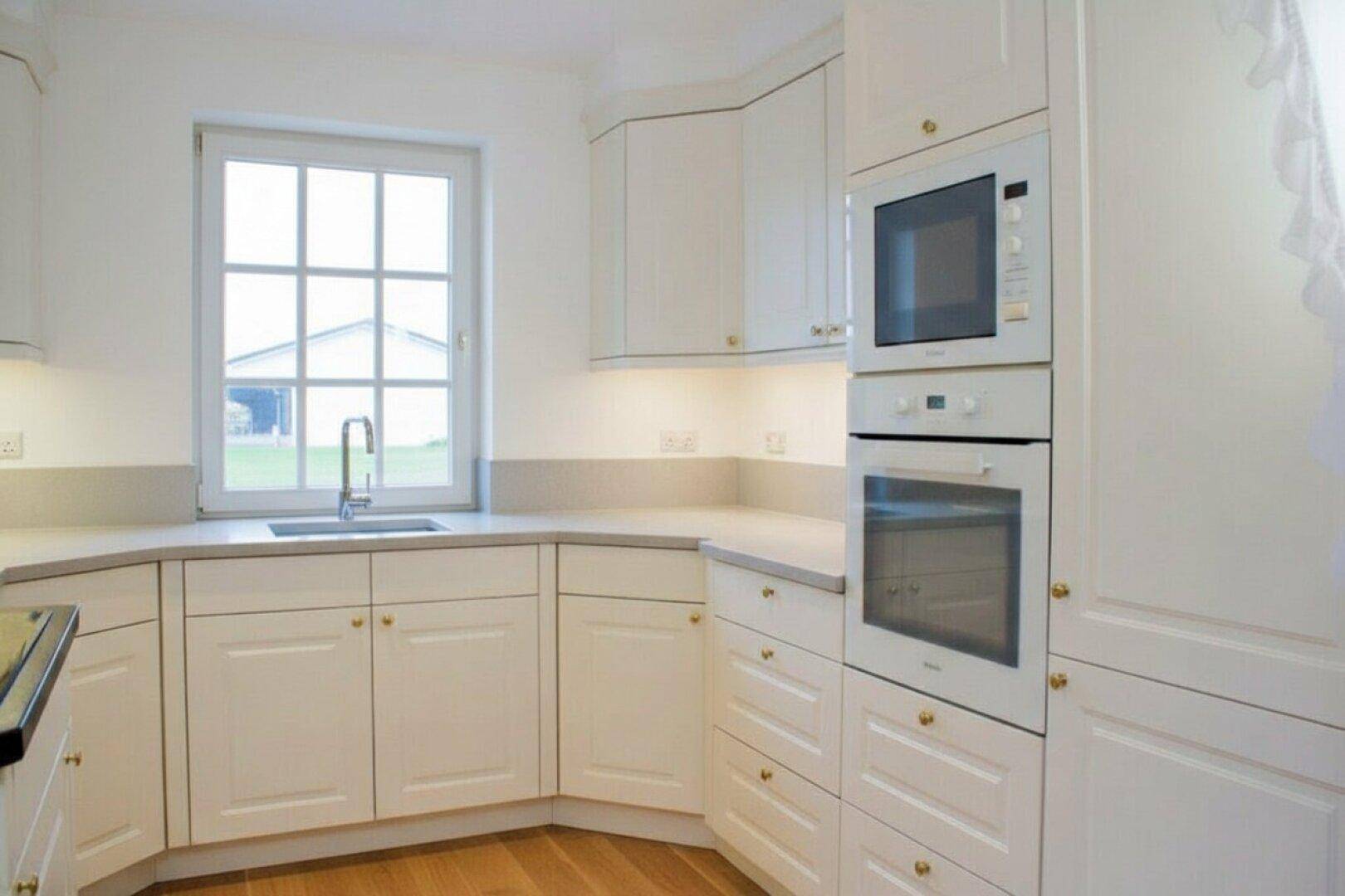Helle Einbauküche in Weiß mit integriertem Backofen und Mikrowelle sowie Fenster.