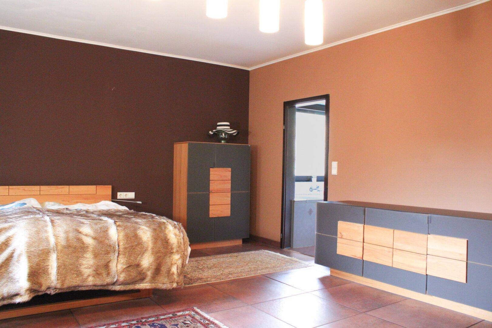 Geräumiges Schlafzimmer mit Holzbett, Kommoden und Zugang zu einem weiteren Raum.
