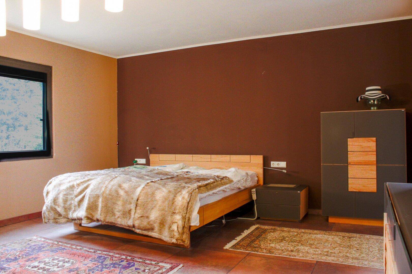 Schlafzimmer mit Holzbett, dunklen Wänden und Fenster mit Blick nach draußen.