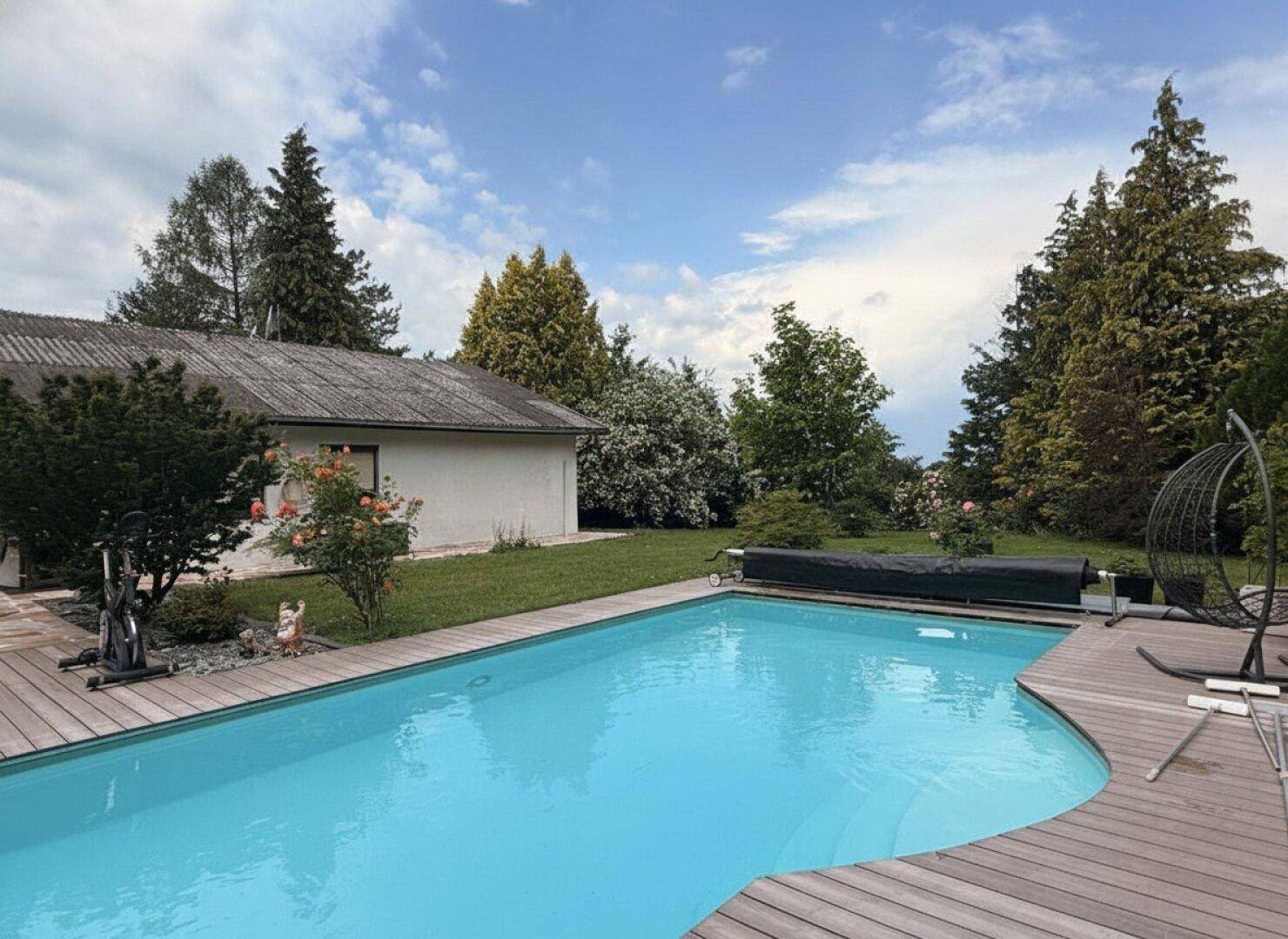 Großer Poolbereich mit Holzdeck und Blick auf das Haus und die grüne Umgebung.