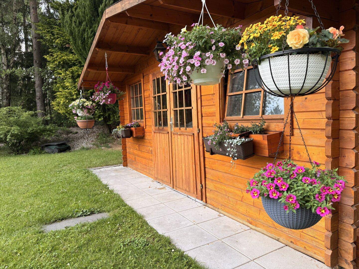 Charmantes Gartenhaus aus Holz mit Blumenampeln und gepflegtem Rasen.