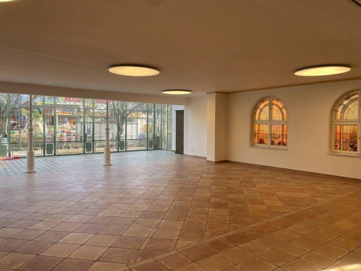 Geräumiger Saal mit Fliesenboden, großen Glasfronten und Rundbogenfenstern, bereit für verschiedene Nutzungen.