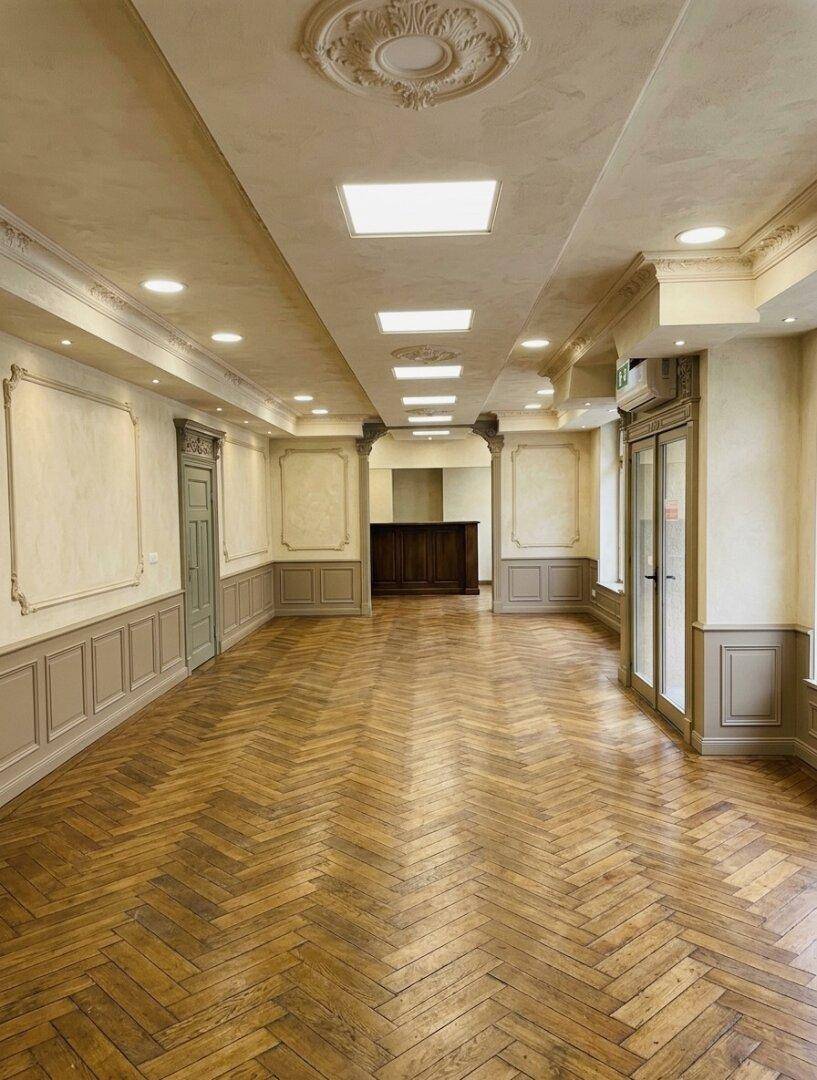 Großer leerer Raum mit Fischgrätparkett, Stuckdecken und eleganten Wandvertäfelungen, ideal für Veranstaltungen.