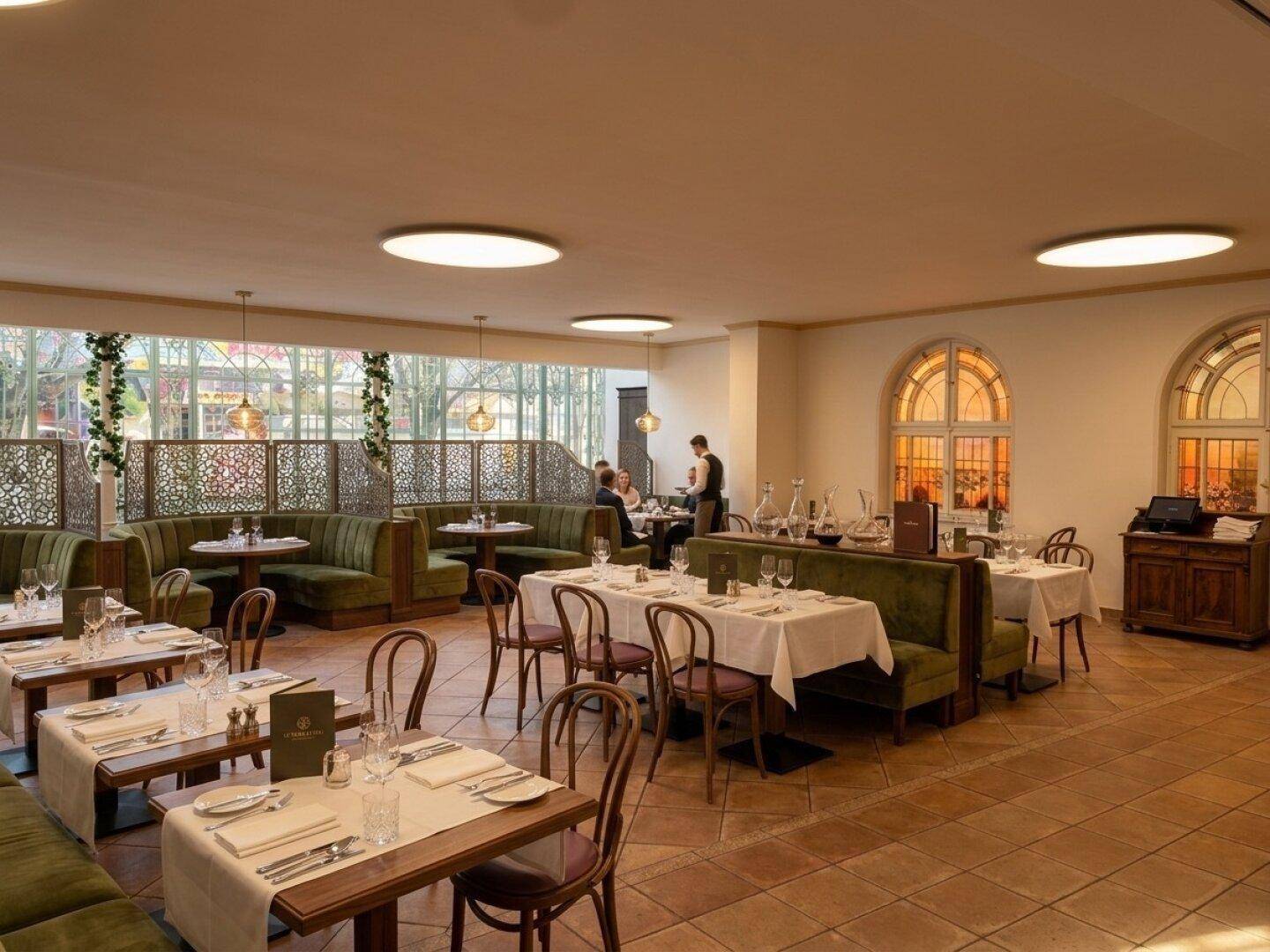 Heller Restaurantbereich mit bequemen grünen Sitzbänken, elegant gedeckten Tischen und großen Rundbogenfenstern.