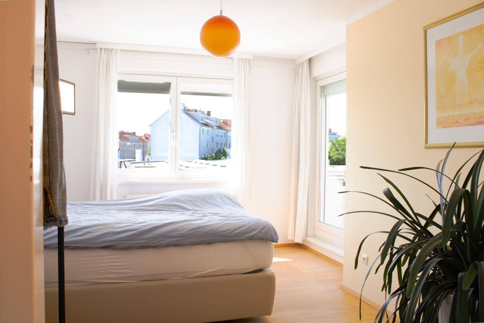 Freundliches Schlafzimmer mit hellem Holzboden, großem Fenster und Zugang zu einem französischen Balkon.