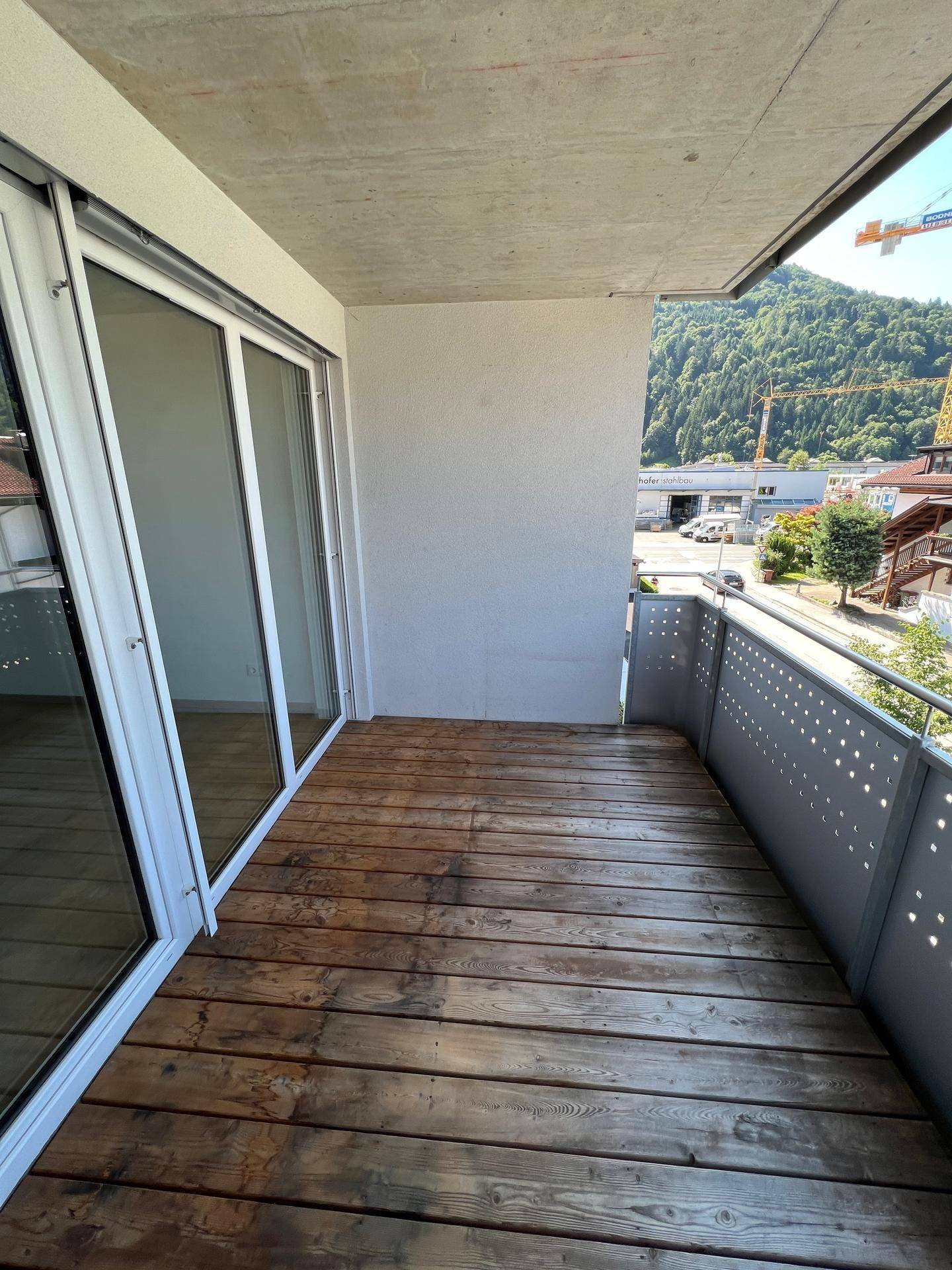Balkon mit Holzdielen und weitem Blick auf die grüne Umgebung und die Berge im Hintergrund.