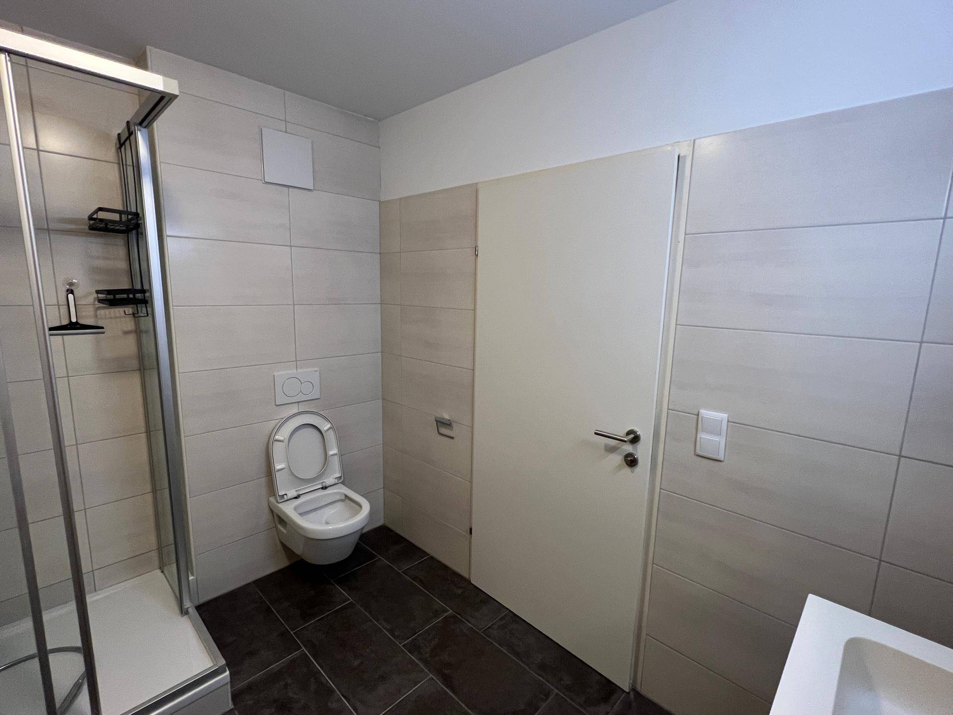 Badezimmer mit Duschkabine, wandhängendem WC und hellen Wandfliesen, funktional und sauber.