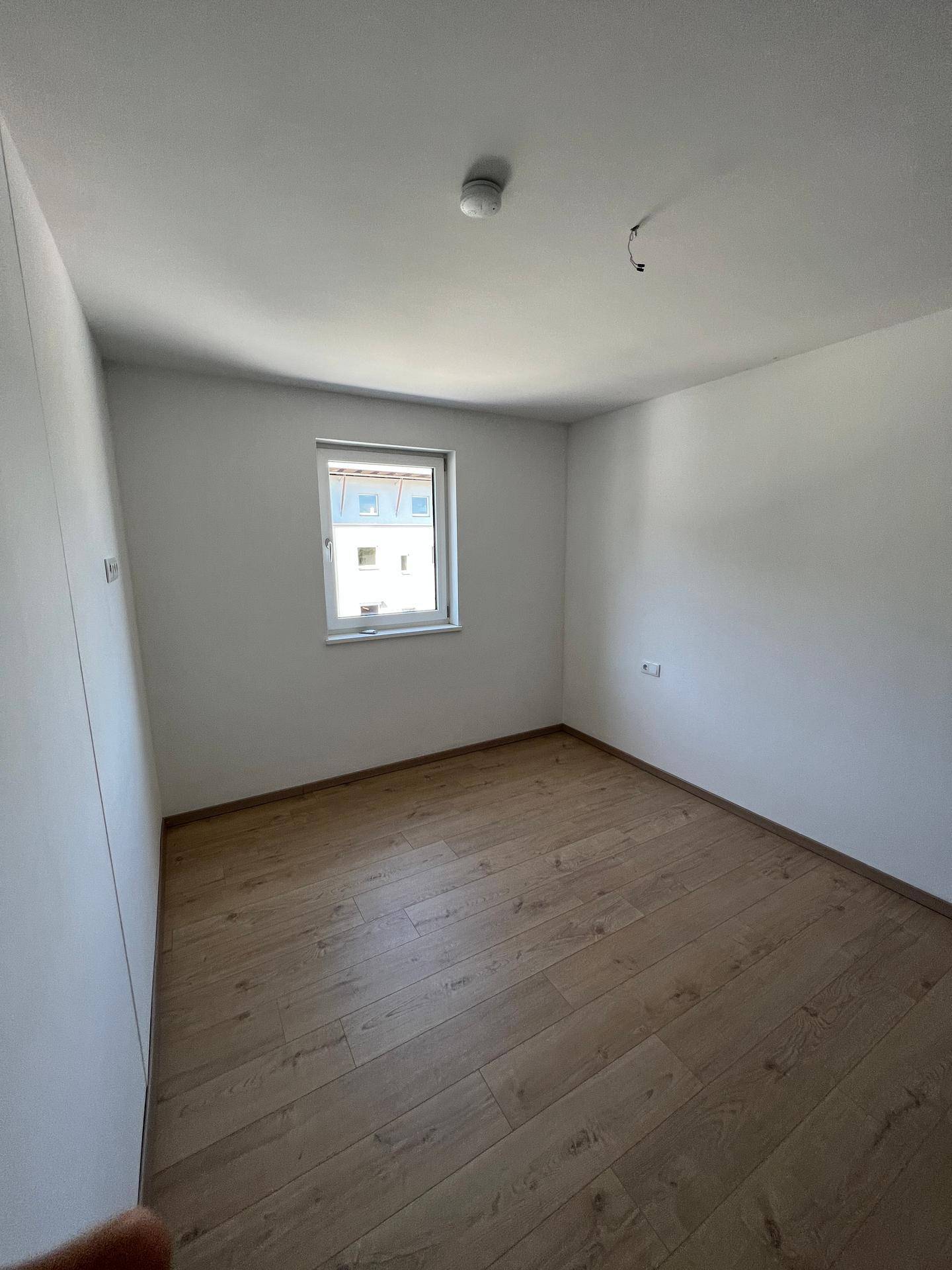 Leeres Zimmer mit Holzboden und einem Fenster, ideal als Schlaf- oder Arbeitszimmer.