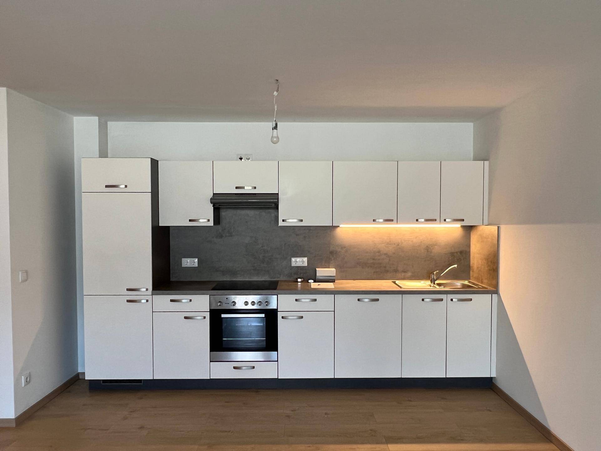 Moderne Einbauküche mit weißen Schränken, integrierten Geräten und dunkler Arbeitsplatte.