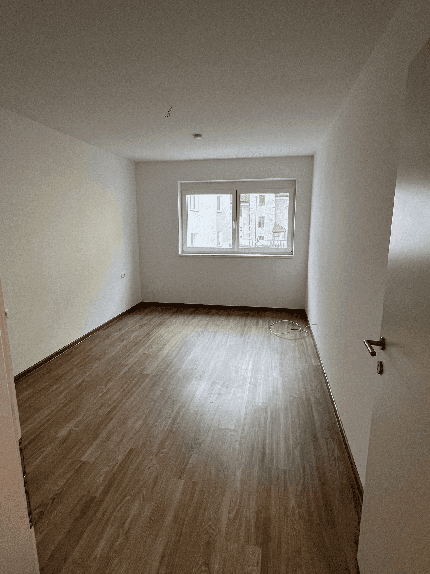 Leeres Zimmer mit Laminatboden und Fenster, geeignet als Schlaf- oder Arbeitszimmer.