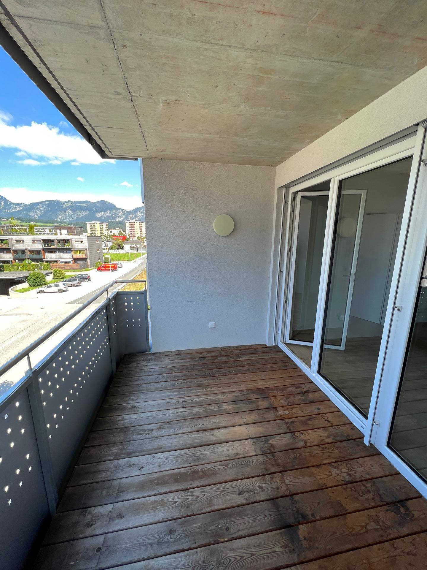 Geräumiger Balkon mit Holzboden und weitem Blick auf die umliegende Berglandschaft und Stadt.
