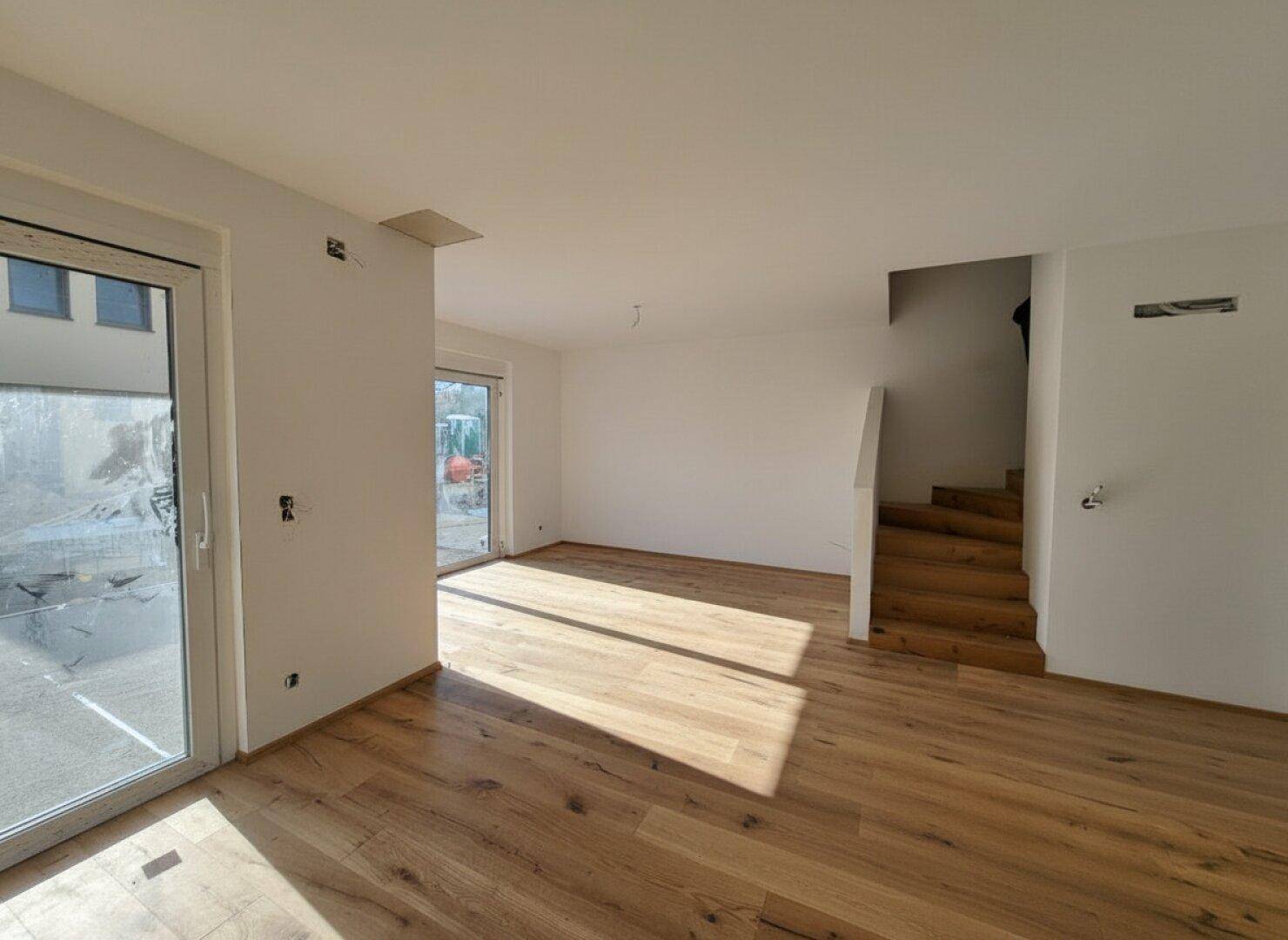 Heller Wohnraum mit Holzboden und großen Schiebetüren, die viel Tageslicht hereinlassen.