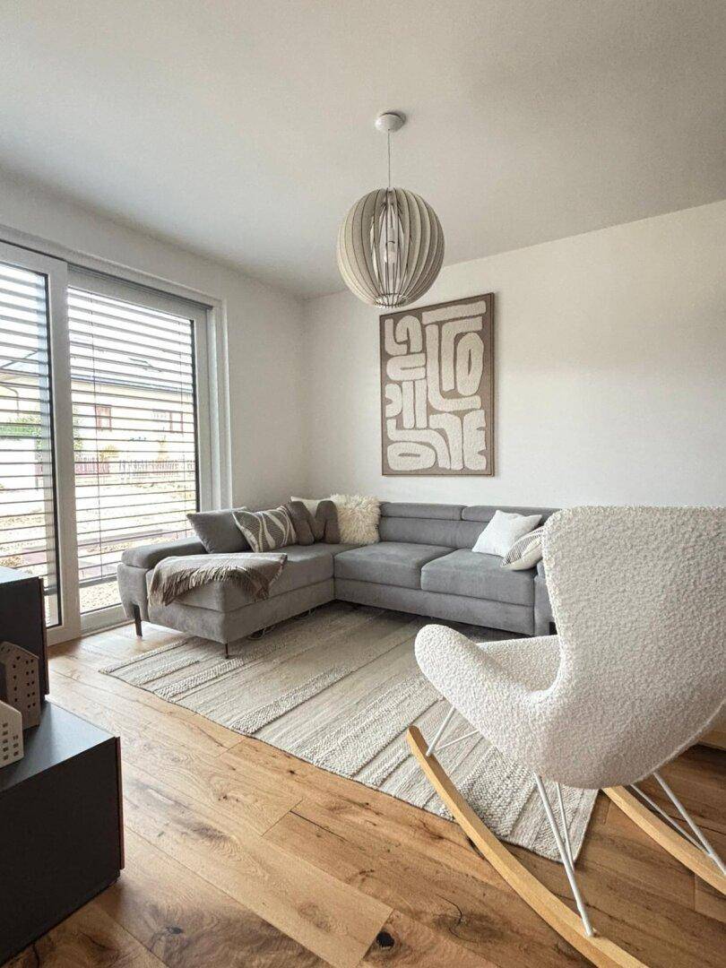 Gemütliches Wohnzimmer mit modernem Sofa, Holzboden und großem Fenster mit Jalousien.