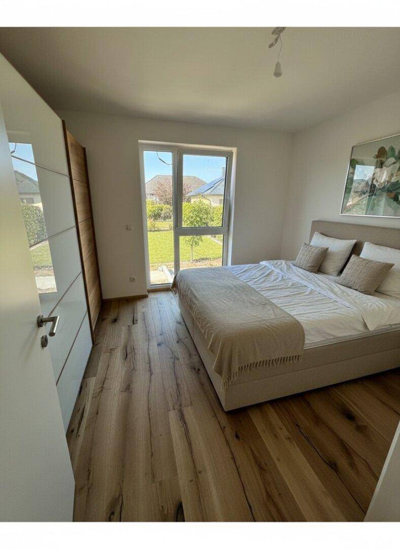 Schlafzimmer mit Holzboden, großem Fenster und Zugang zum Gartenbereich.