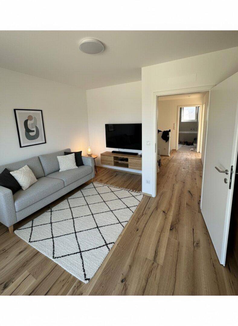 Wohnzimmer mit bequemem Sofa, Fernseher und Holzboden, führt zu einem weiteren Raum.