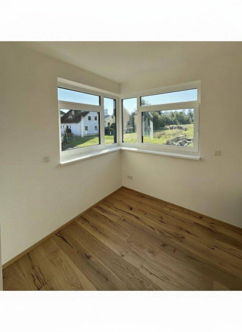 Helles Zimmer mit Holzboden und Eckfenstern, bietet einen weiten Blick ins Grüne.
