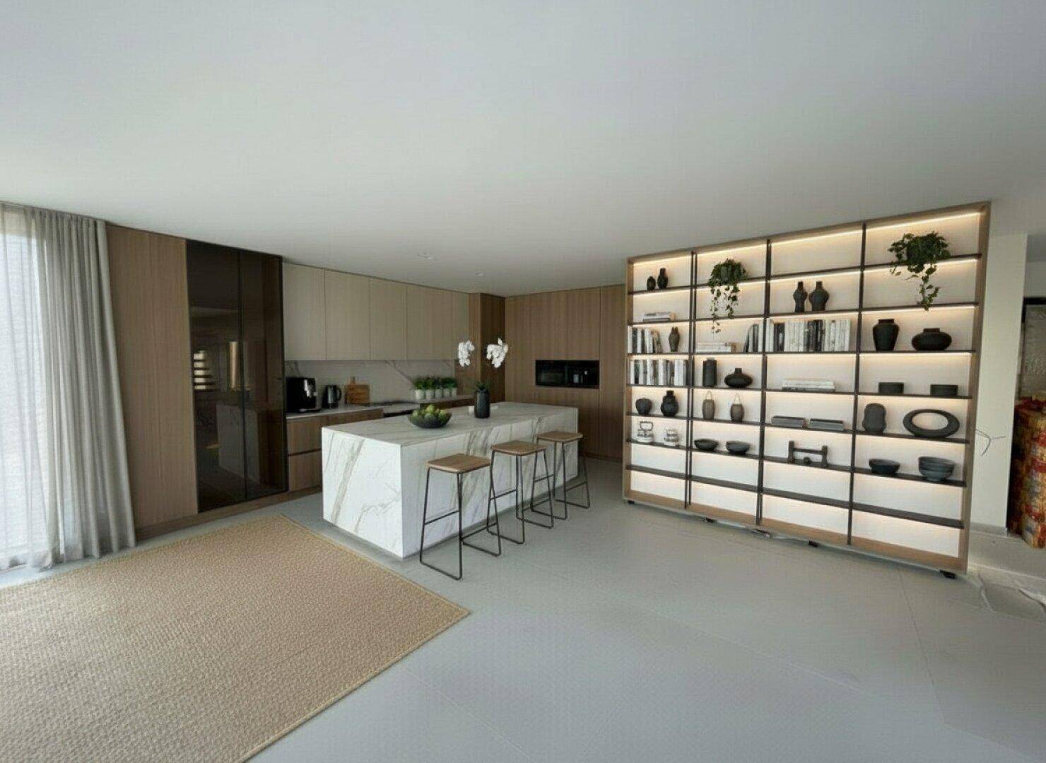 Moderne Küche mit großer Kochinsel, integrierten Geräten und beleuchtetem Regal als Raumteiler.